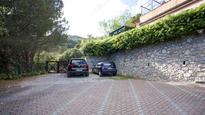 Ein gepflasterter Weg mit zwei parkenden Autos, einer Steinmauer und einem Gebäude mit Gründach.