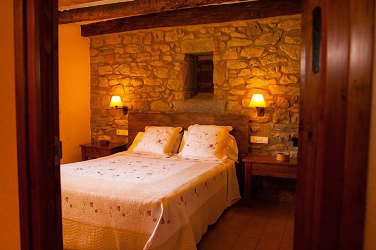 Une chambre confortable avec un mur en pierre, deux lampes de chevet et un lit soigneusement fait.