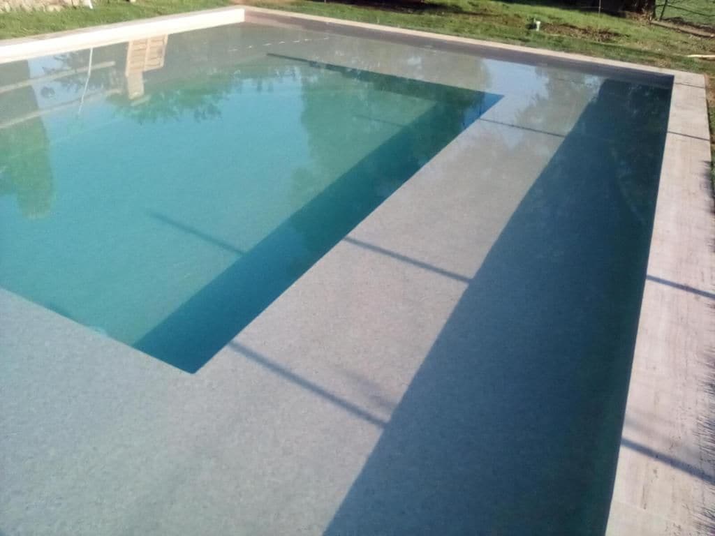 Una piscina con agua cristalina, rodeada por una solera de hormigón.