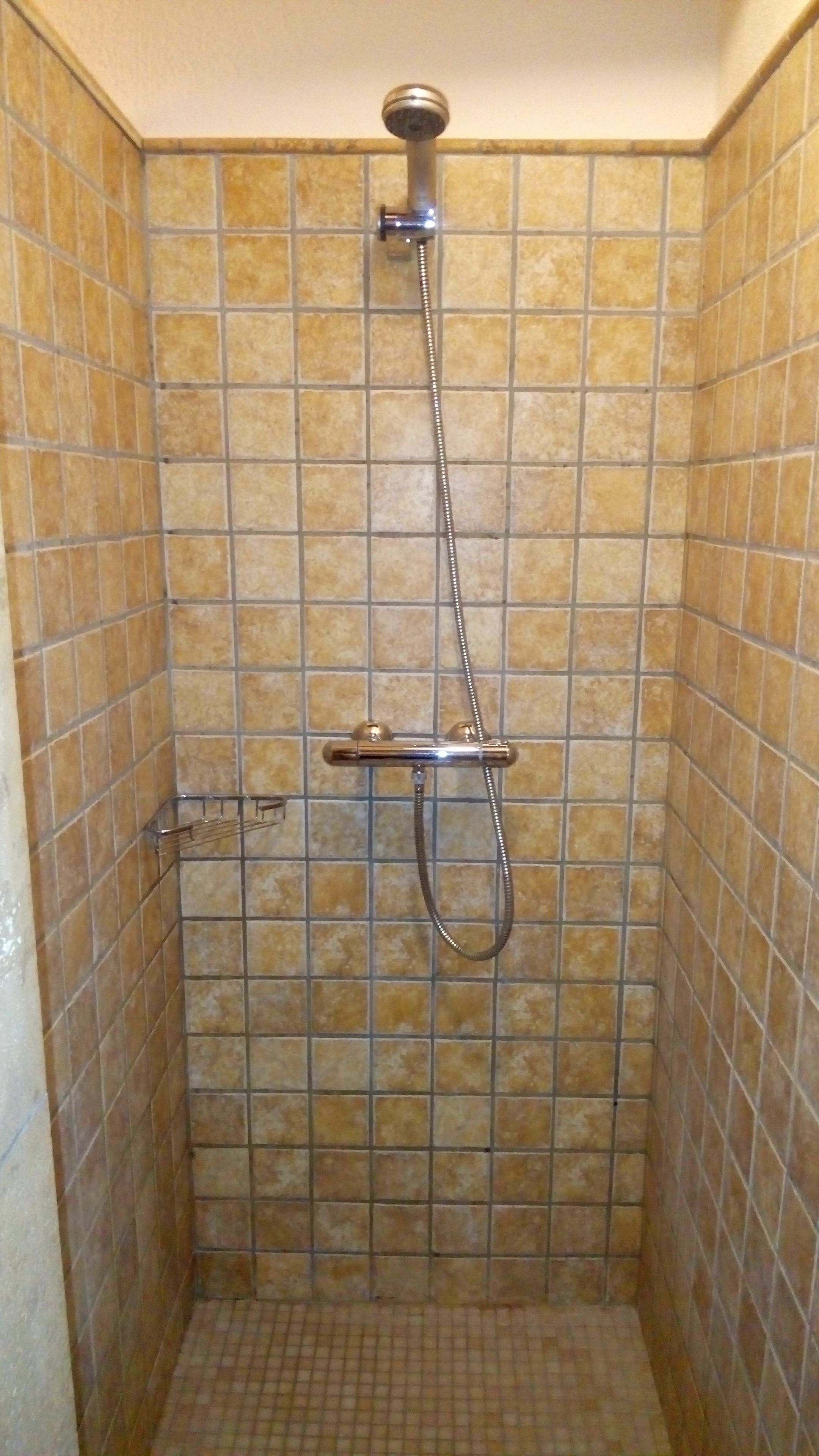 A small, tiled shower stall with a handheld showerhead and a handheld shower attachment.