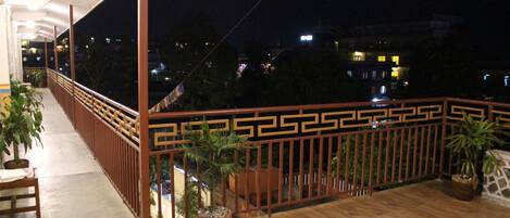 Un balcón con piso de madera, plantas en macetas y barandilla decorativa.
