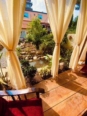 A patio area with a view of a garden, a wooden table, and a red chair. - Three Jewels Boutique Hotel (Pokhara)