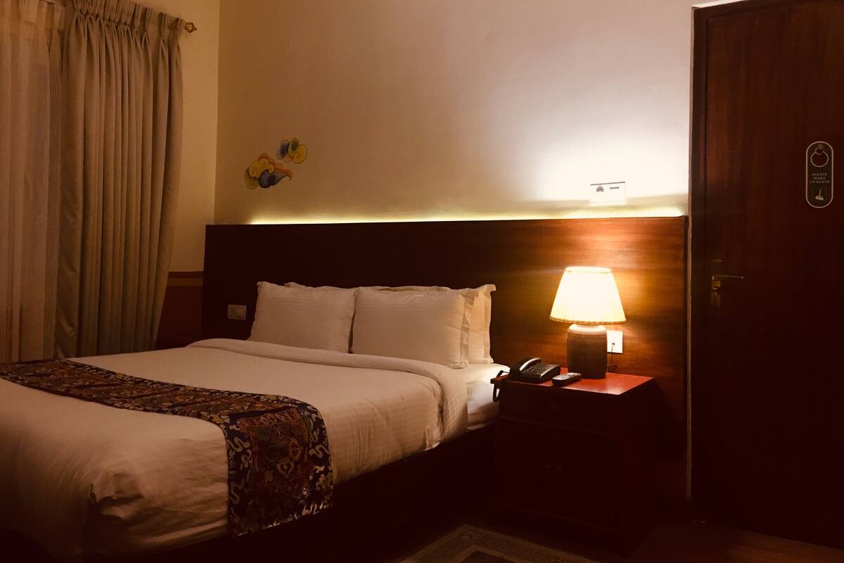 A hotel room with a large bed, a bedside lamp, a telephone, and a door with a sign.