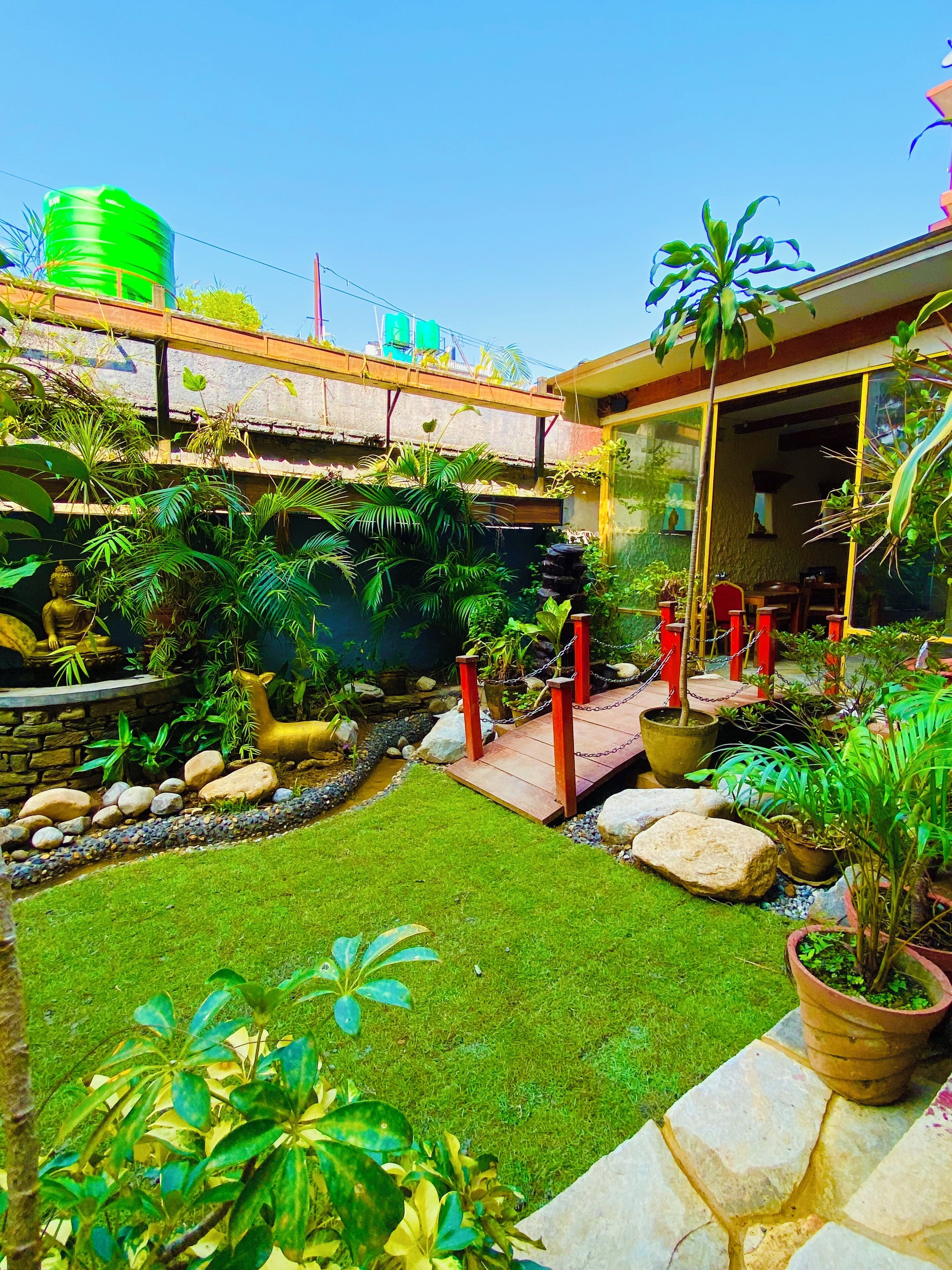 A well-maintained garden with a variety of plants, a small bridge, and a statue.
