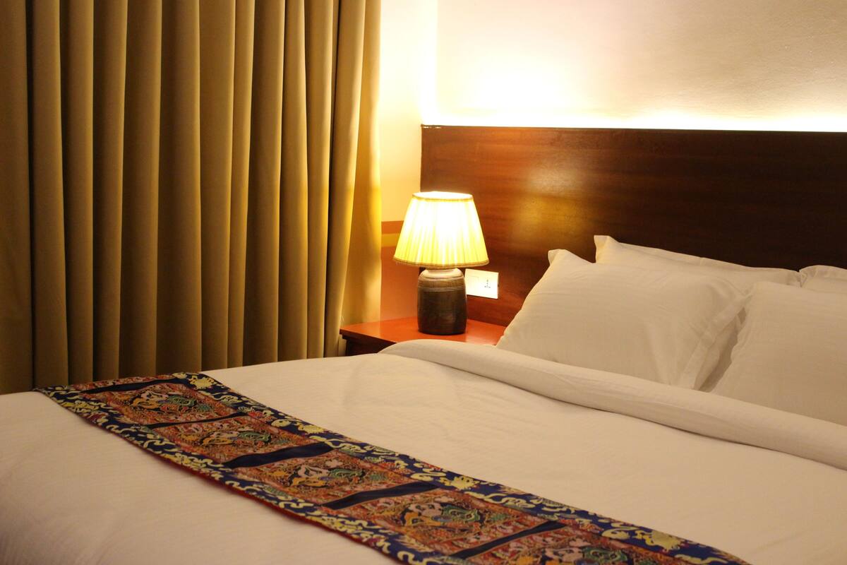 A hotel room with a bed, a nightstand, a lamp, and a window with curtains.