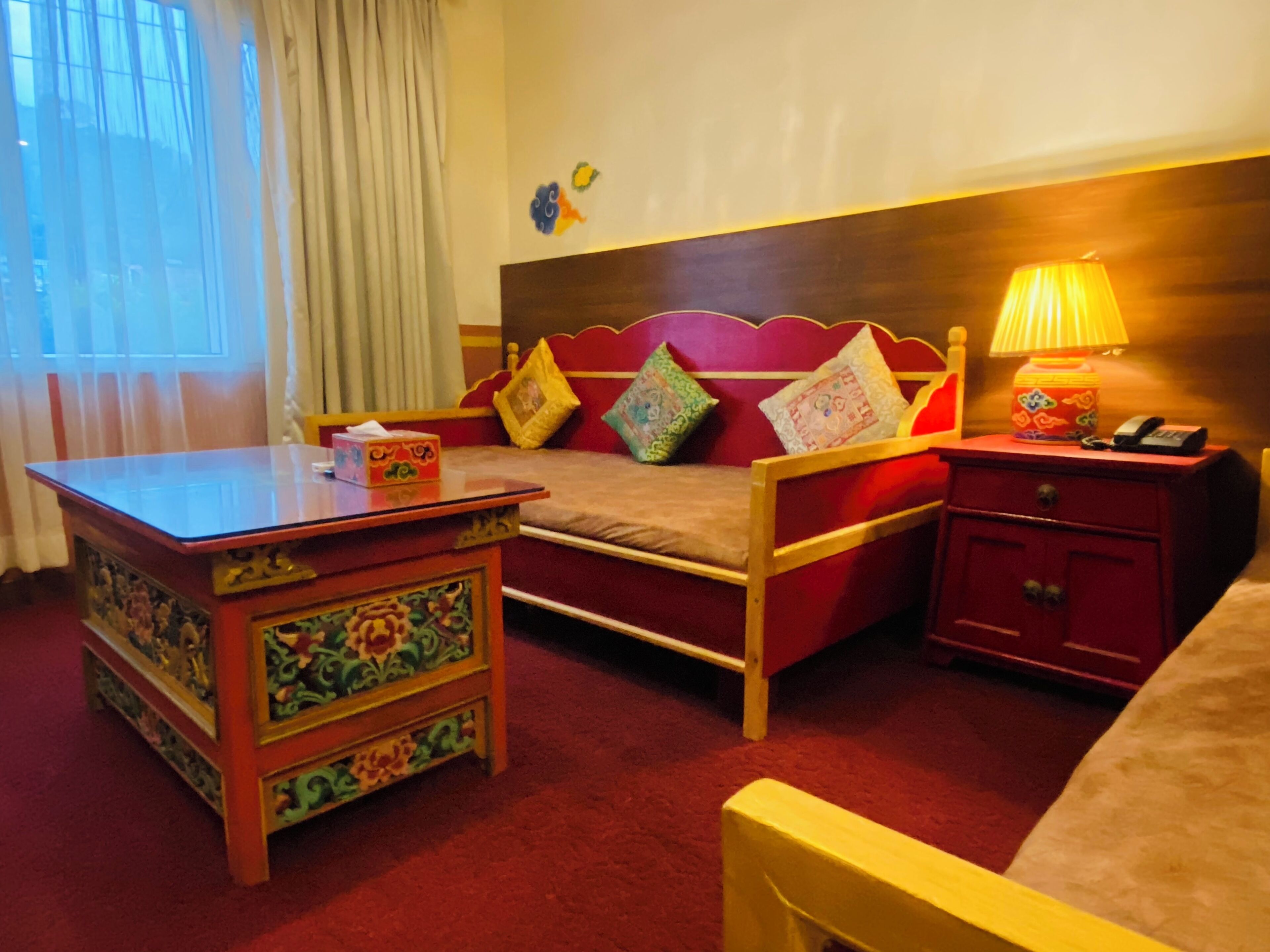 A hotel room with a bed, a bedside table, a nightstand, and a window with curtains.