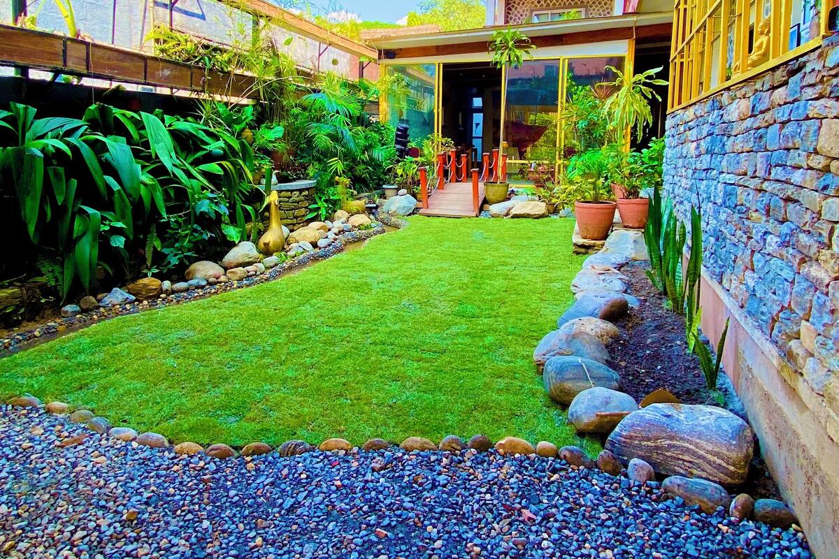 A modern building with a glass entrance, a stone wall, and a well-maintained garden with pebbles and plants.