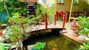 En dam med koi-karper og en træbro, omgivet af plantekrukker og sten.