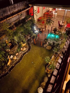 Un jardín interior con un pequeño estanque, cubierta de madera y diversas plantas en macetas.