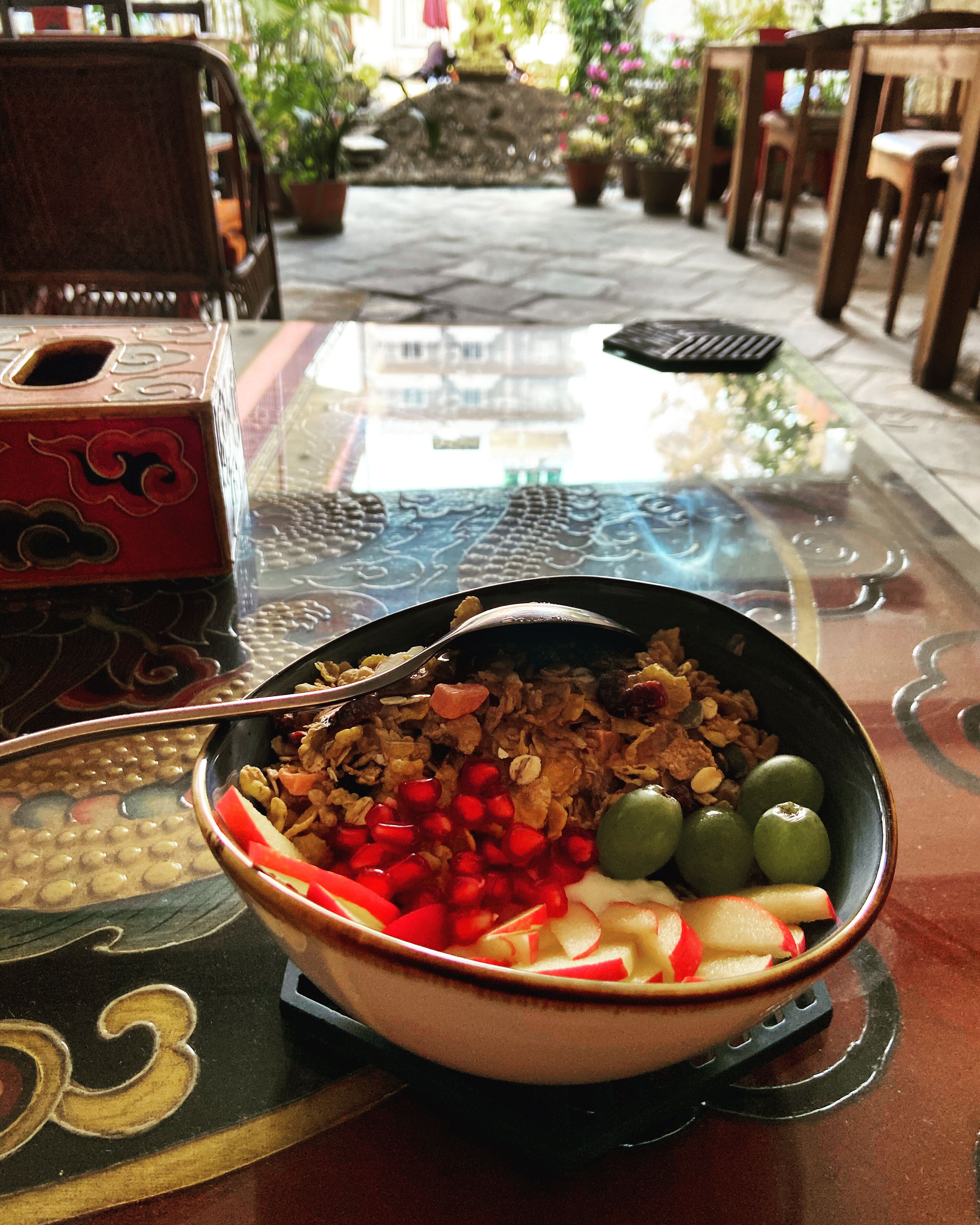 A bowl of cereal with fruits and granola on a table with a glass top.