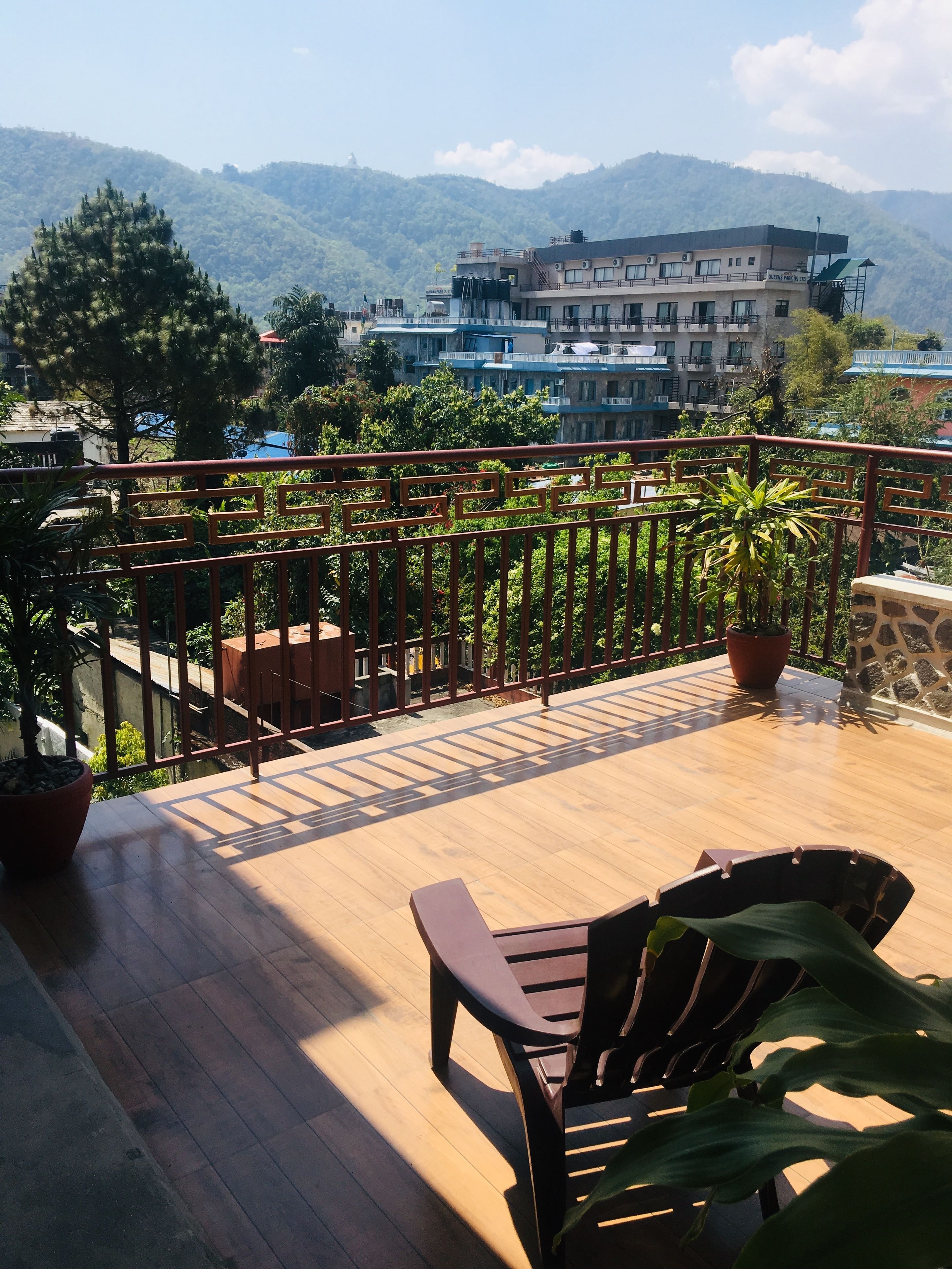 A wooden deck with a metal railing, potted plants, and a view of a mountainous landscape.