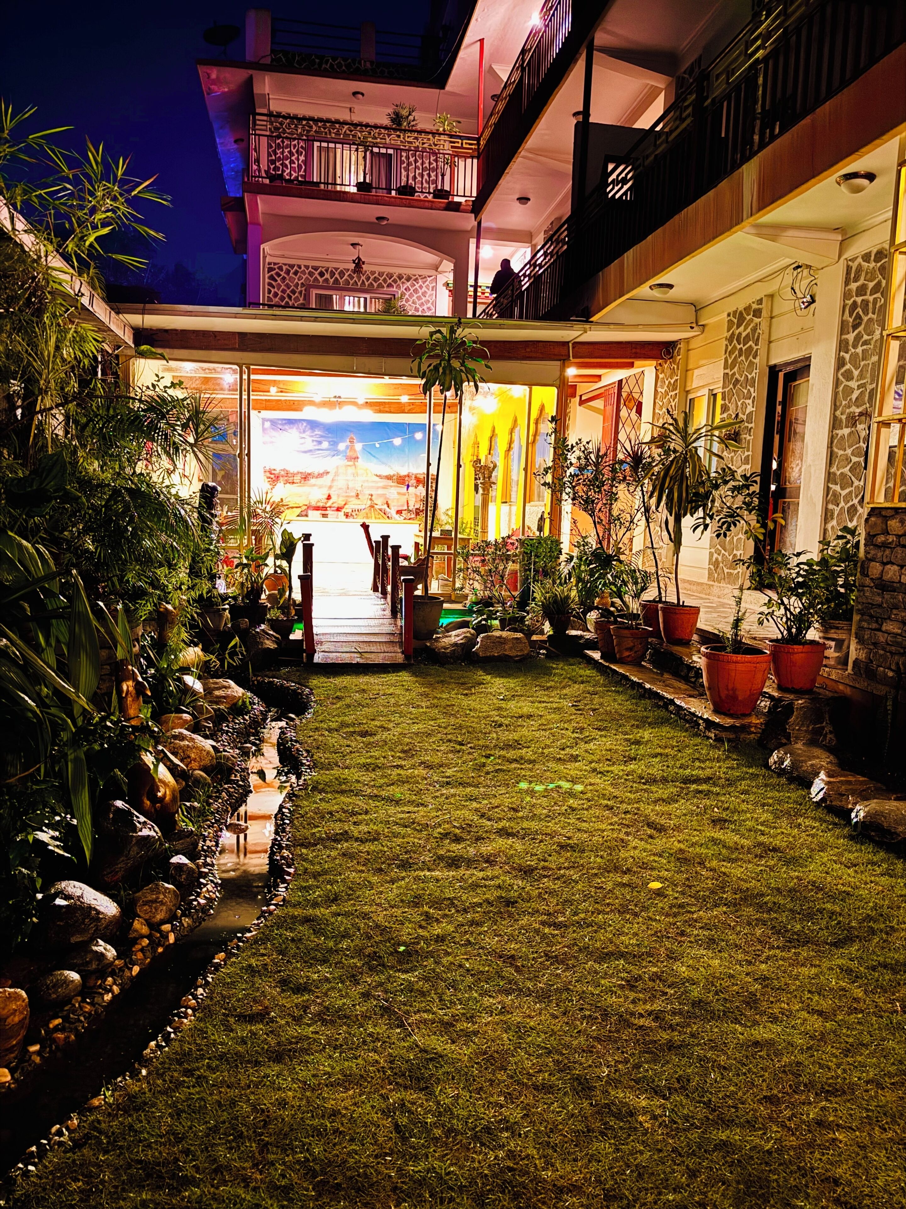 A well-maintained outdoor area with a pathway leading to a building entrance, surrounded by potted plants and a small rock garden.