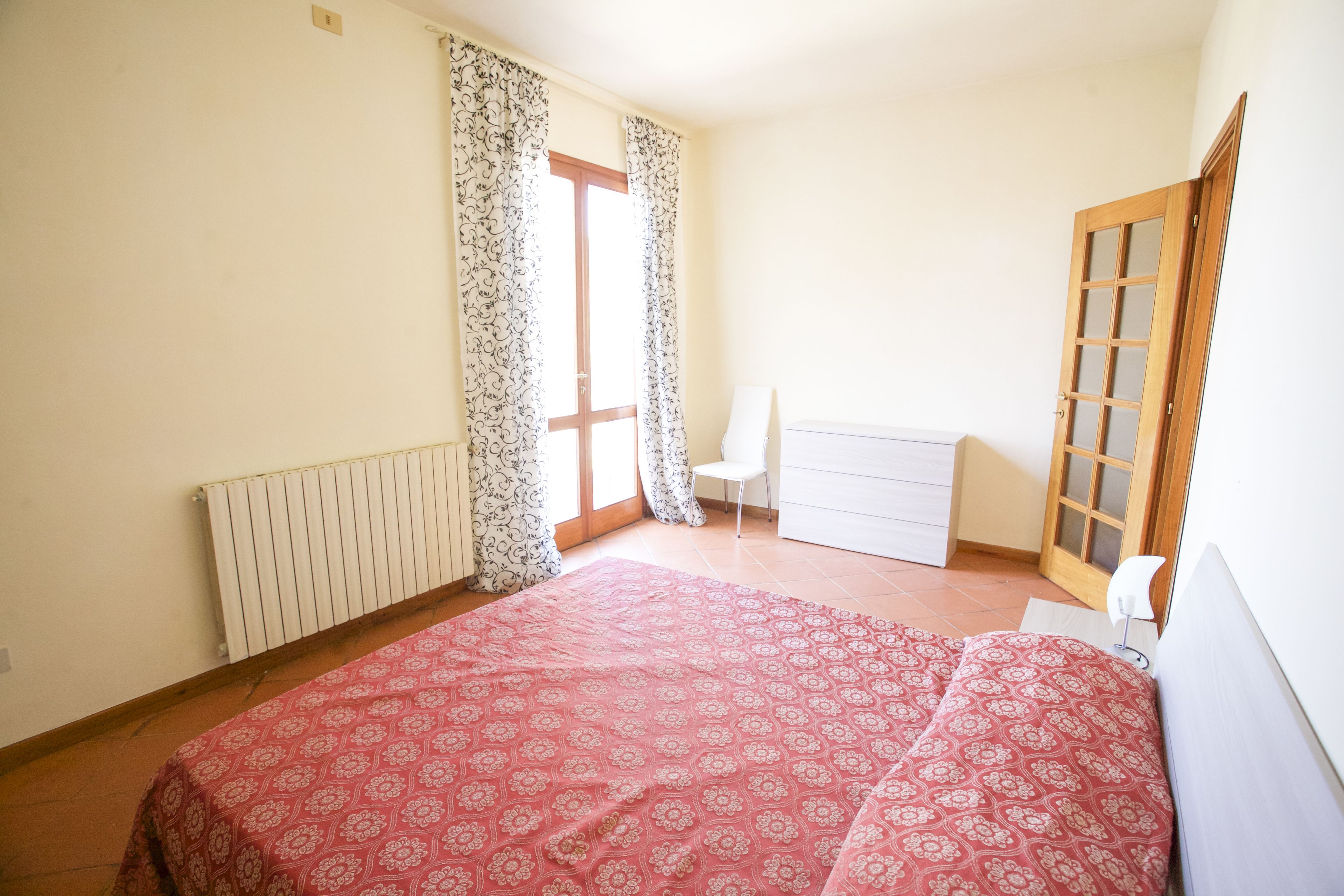 A bedroom with a bed, a chair, a dresser, and a window with curtains.