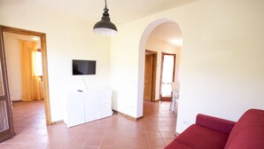 A spacious living area with a red sofa, a television mounted on the wall, and a tiled floor. - Villino Laura (Portoferraio)