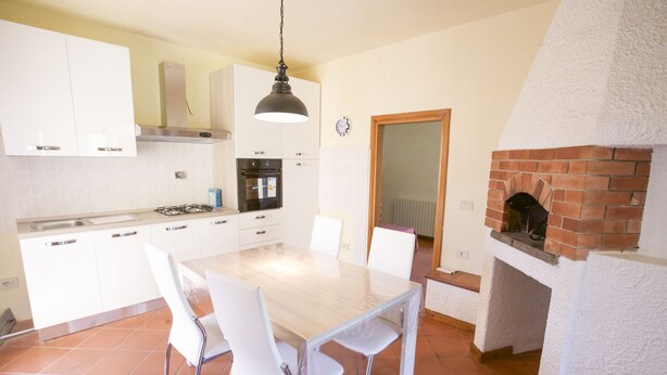 A kitchen with white cabinets, a wooden table, and chairs, a gas stove, and a brick fireplace. - Villino Laura (Portoferraio)