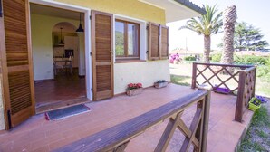 An open wooden door leading to a kitchen with a dining area, a patio with wooden railings, and potted plants. - Villino Laura (Portoferraio)