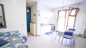 Un espacio habitable compacto con kitchenette, una zona de comedor con mesa y sillas, y una cama con colcha estampada.