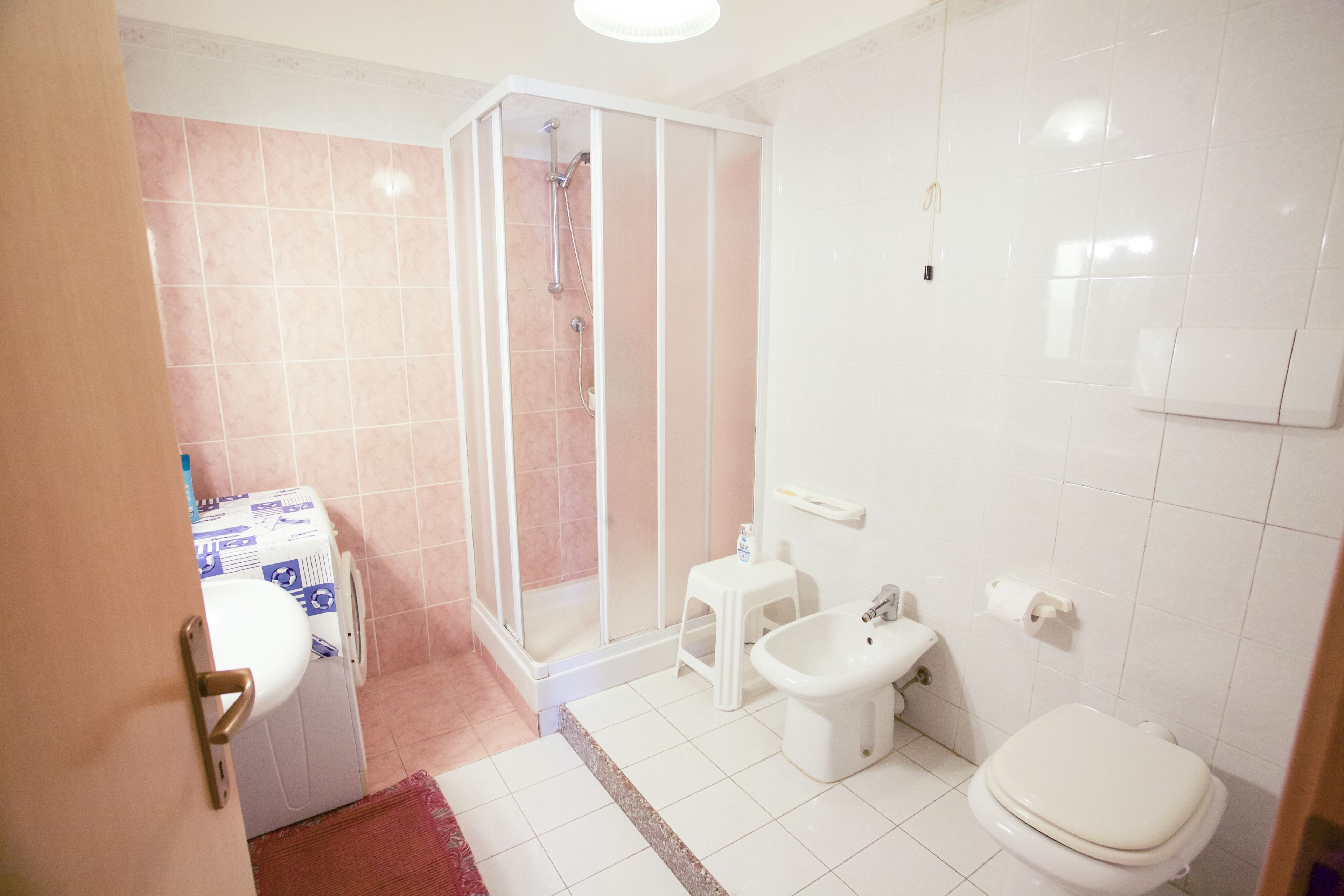A bathroom with a shower, toilet, bidet, and a small stool.