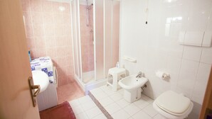 Un baño con ducha, inodoro, bidé y un taburete pequeño.