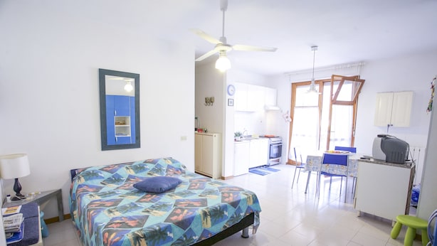Un dormitorio con cama, escritorio, silla, kitchenette y baño.