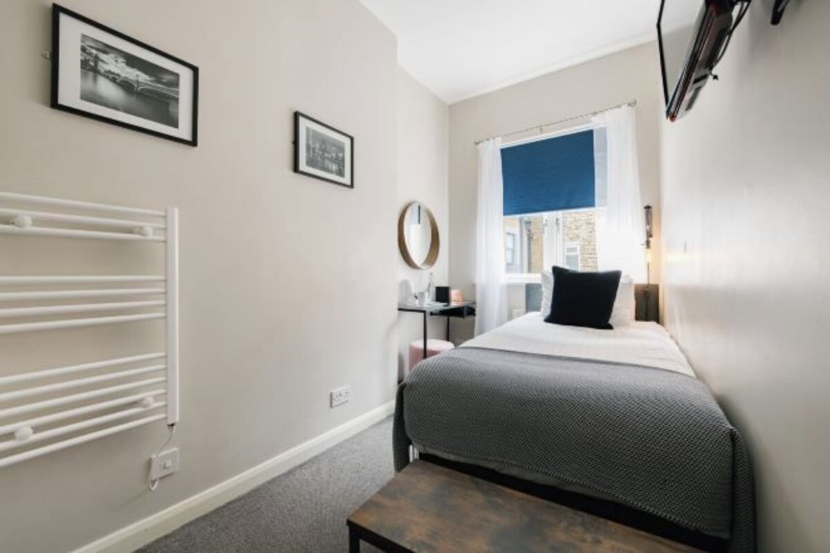 A bedroom with a bed, a bedside table, a mirror, and a radiator.
