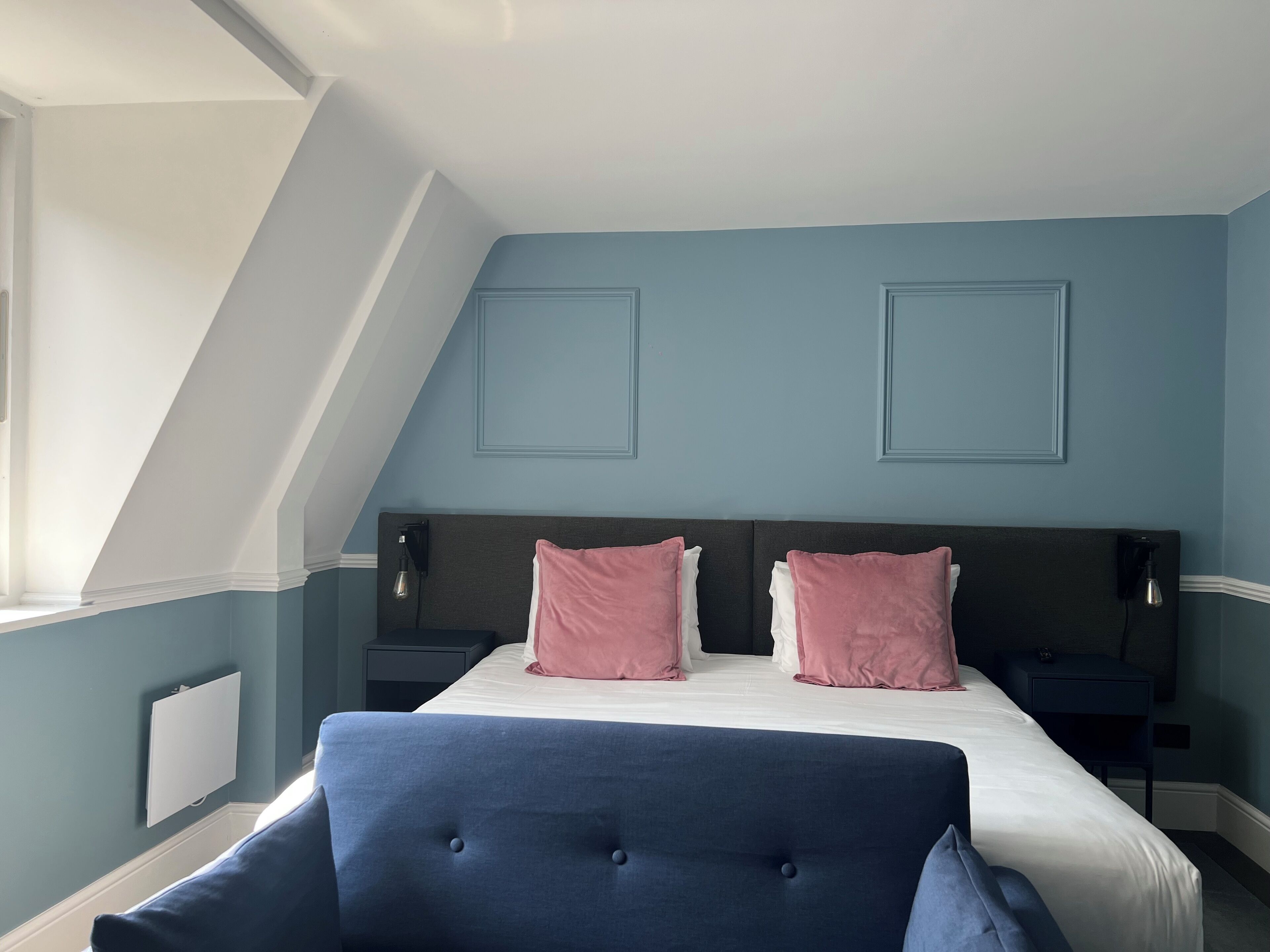 A bedroom with a bed, two nightstands, a chair, and a sloped ceiling.