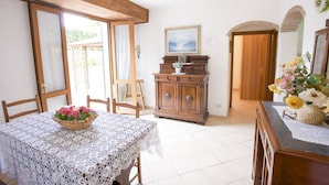 A dining area with a table set for two, a wooden cabinet, and a door leading to another room. - Appartamento La Casina (Portoferraio)