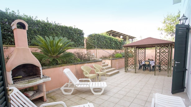 A patio with a pizza oven, lounge chairs, and a covered seating area. - Appartamento La Casina (Portoferraio)