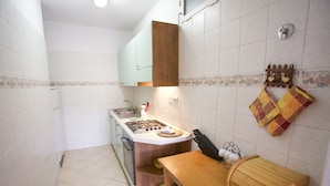 A compact kitchen with white tiled walls, a wooden countertop, and a small dining table. - Appartamento La Casina (Portoferraio)