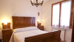 A bedroom with a wooden bed, two bedside tables with lamps, a chandelier, and a window with curtains. - Appartamento La Casina (Portoferraio)