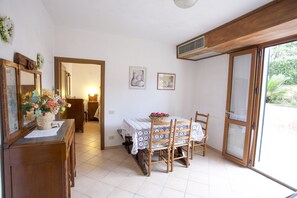 A dining area with a table set for four, wooden chairs, a vase with flowers, and two framed pictures on the wall. - Appartamento La Casina (Portoferraio)