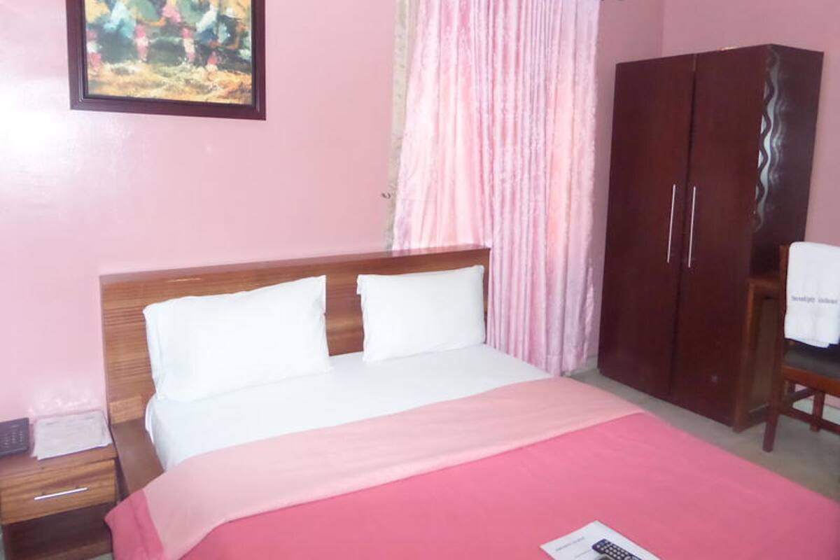 A bedroom with a bed, a wardrobe, a painting on the wall, and a curtain.