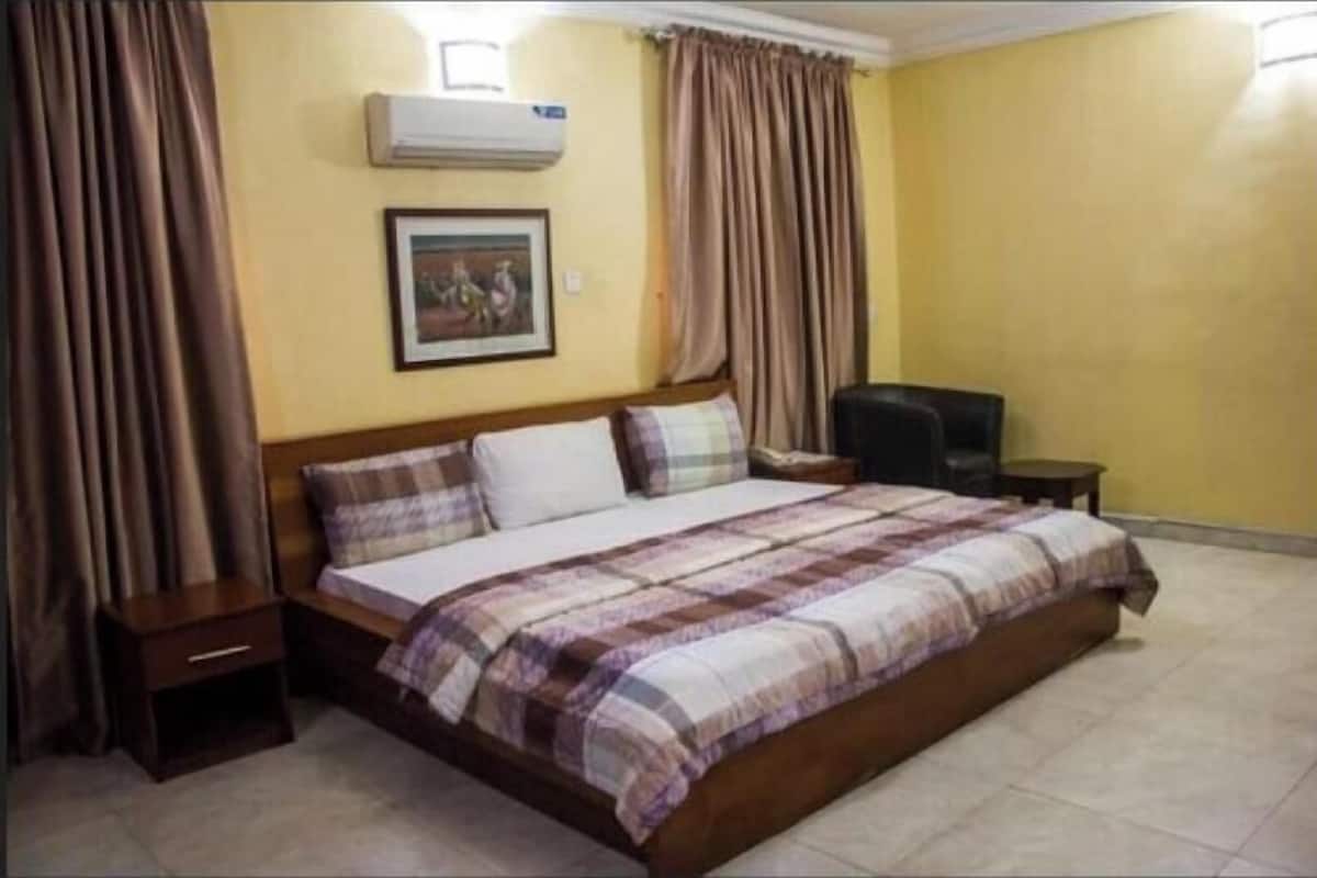 A bedroom with a bed, a nightstand, a chair, a picture on the wall, and curtains.