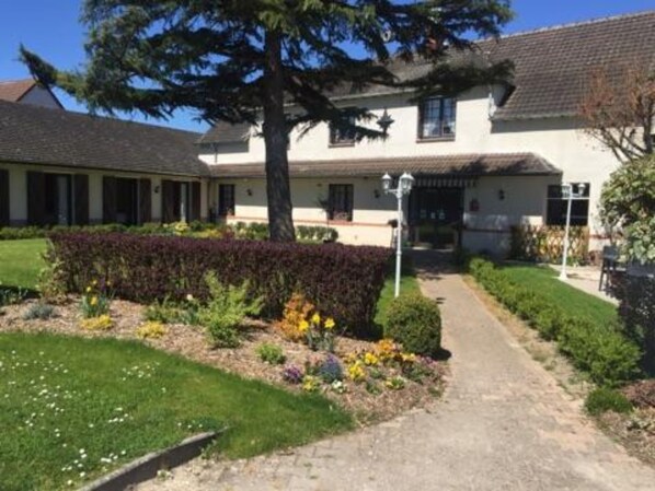 A two-story building with a covered porch, a pathway leading to the entrance, and a well-maintained garden with various plants and flowers. - Le Lanthenay (Romorantin-Lanthenay)