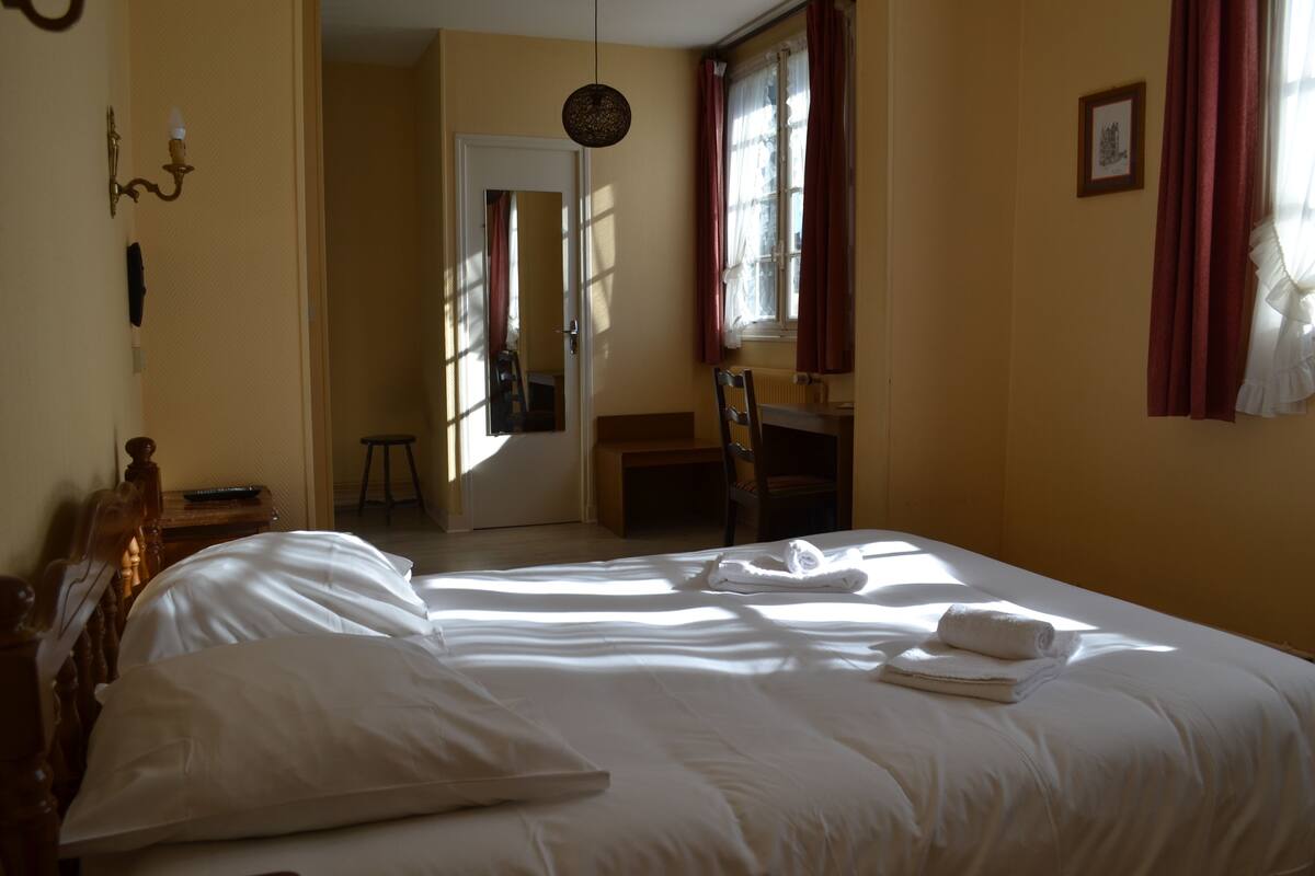 Ein Hotelzimmer mit einem großen Bett, einem Nachttisch aus Holz, einem Sessel und einem Schreibtisch.