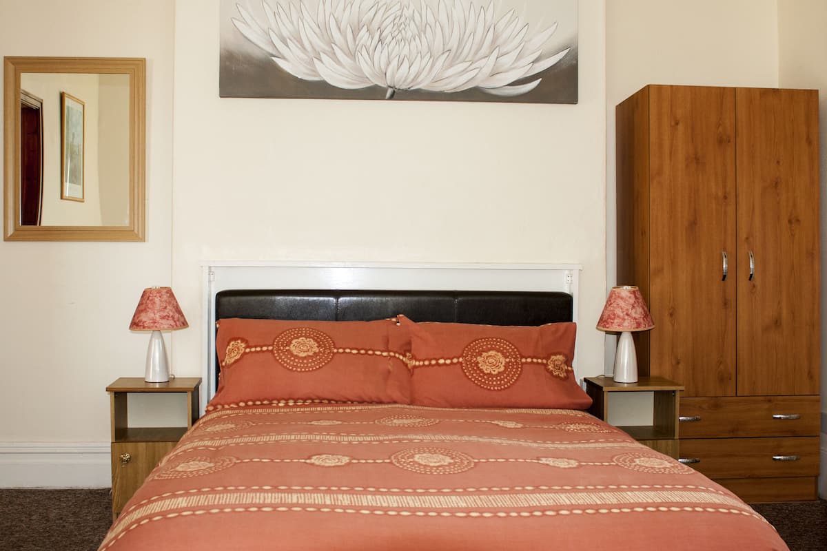 A bedroom with a bed, two bedside tables with lamps, a wardrobe, and a wall-mounted painting.
