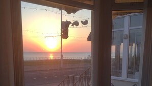 A room with a large window overlooking a sunset, a small table, and two wicker chairs. - Adelphi Holiday Flats (Blackpool)
