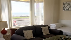 A hotel room with a sofa, a small table, a bed, and a window with a view of the sea. - Adelphi Holiday Flats (Blackpool)