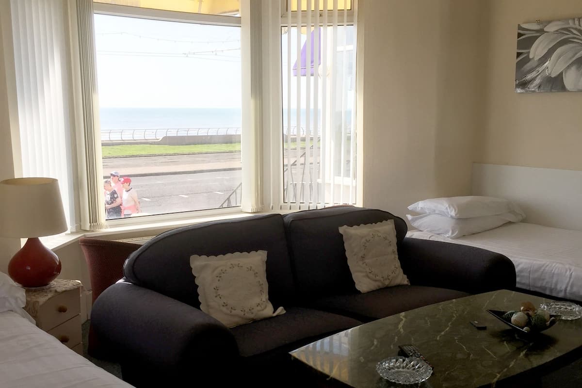 A hotel room with a sofa, a small table, a bed, and a window with a view of the sea.