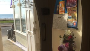 A hotel entrance with a view of the sea, a bulletin board with event posters, and a flower vase. - Adelphi Holiday Flats (Blackpool)