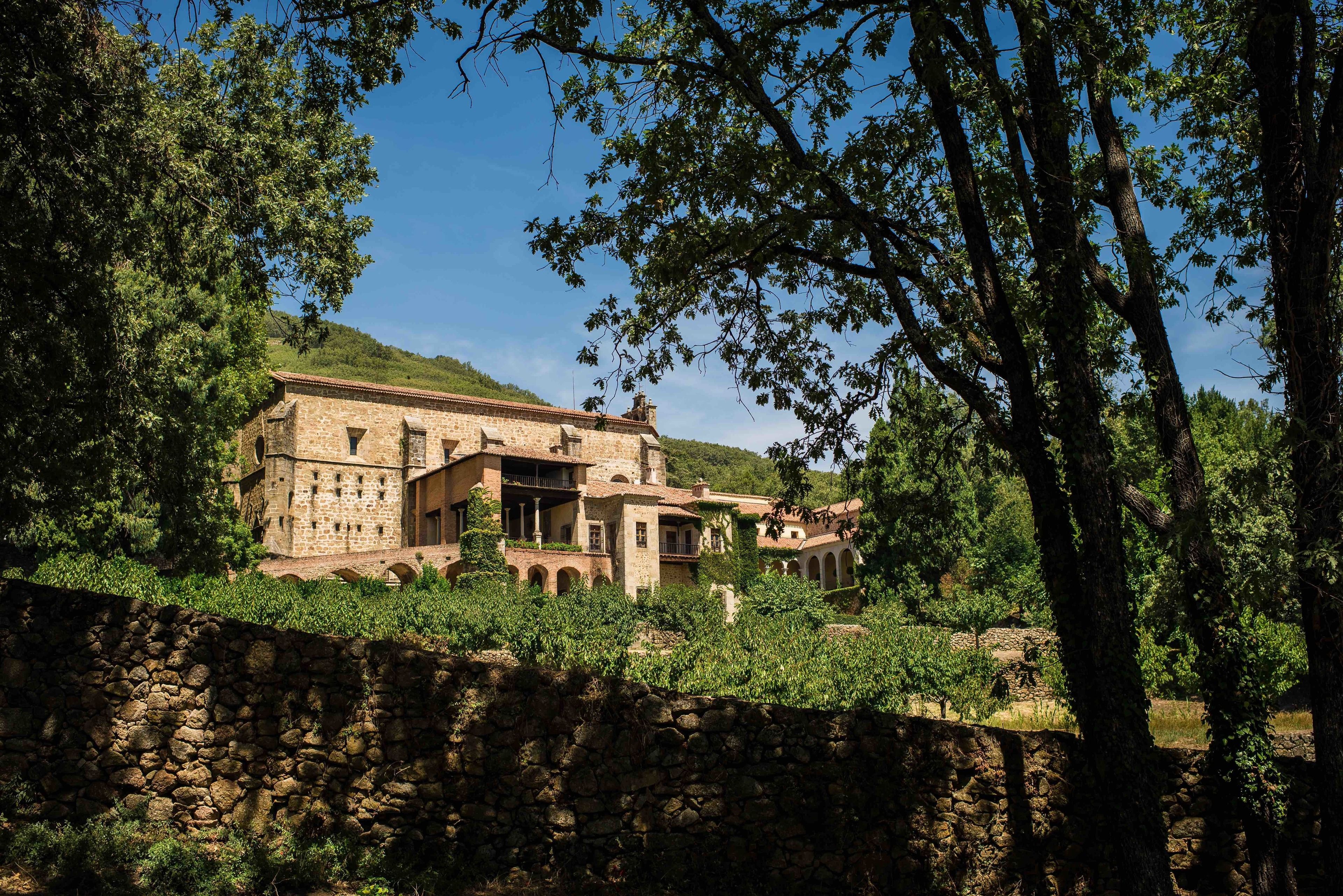 Un edificio de piedra con múltiples arcos y un patio interior, rodeado de árboles y vegetación.