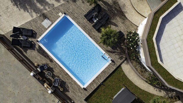 An aerial view of a swimming pool with lounge chairs and a table, surrounded by a paved area and greenery. - Villa Paradise (Rhodes)