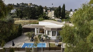 A modern villa with a swimming pool, outdoor seating, and a view of the surrounding landscape. - Villa Paradise (Rhodes)
