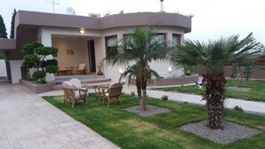 A modern house with a patio area featuring outdoor furniture and a well-maintained lawn. - Villa Paradise (Rhodes)