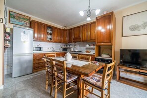 A kitchen with wooden cabinets, a refrigerator, a dining table with chairs, a television, and a tiled backsplash. - Appartamento Clara Vista Mare (Campo nell'Elba)
