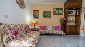 A living room with a floral sofa, a wooden cabinet, and a lamp. - Appartamento Clara Vista Mare (Campo nell'Elba)