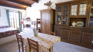 A dining area with a wooden table and chairs, a cabinet with glass doors, and a bed with a floral bedspread. - Appartamenti Cotoncello (Marciana)