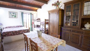 A room with a bed, a table with chairs, a wooden cabinet, and a window with curtains. - Appartamenti Cotoncello (Marciana)