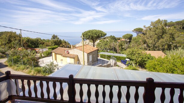 A balcony with a view of a coastal village, including houses, trees, and the sea. - Appartamenti Cotoncello (Marciana)