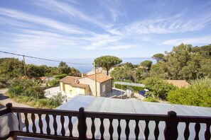 Un balcón con vistas a un pueblo costero, que incluye casas, árboles y el mar.